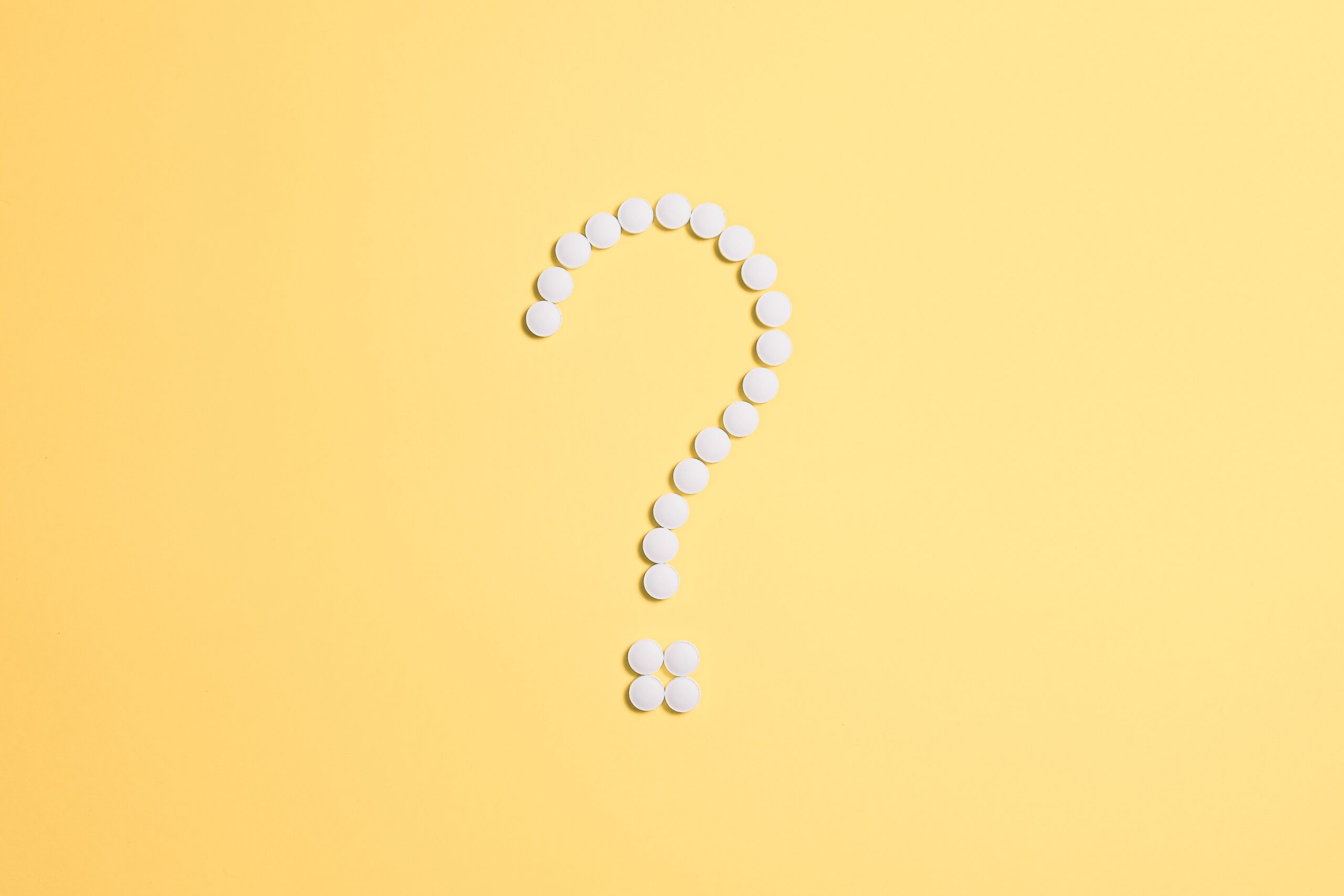 White pills arranged into a question mark shape on a vibrant yellow background.